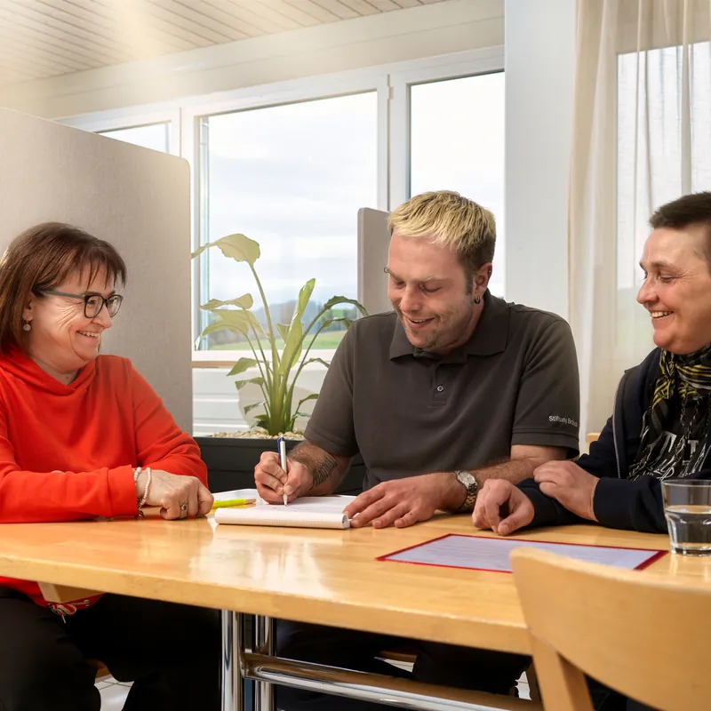 Drei Personen besprechen sich lachend an einem Tisch